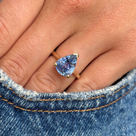 Vintage inspired pear-cut bluebell sapphire solitaire engagement ring with a pear-shaped bluebell sapphire centre stone, photographed on hand against denim.