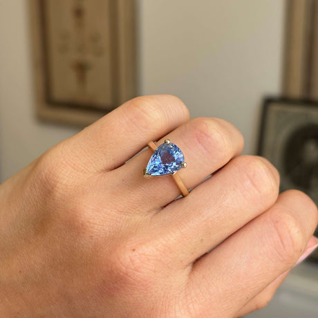 Close-up of a vintage inspired pear-cut bluebell sapphire solitaire engagement ring highlighting the faceted pear-shaped sapphire and elegant yellow gold band.