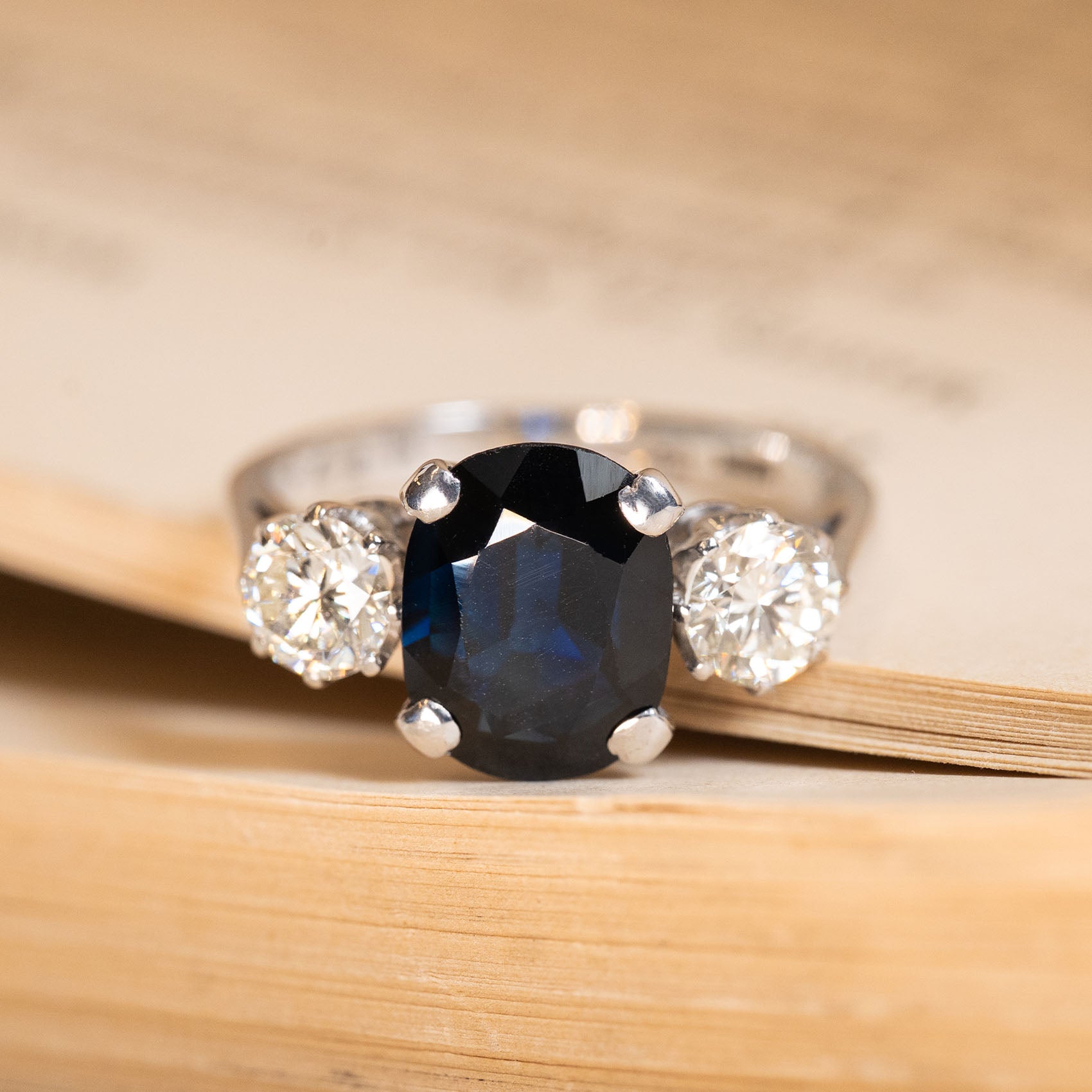 Vintage 1970s midnight-blue sapphire and diamond three-stone ring featuring an oval-cut deep blue sapphire flanked by round brilliant-cut diamonds in white gold.