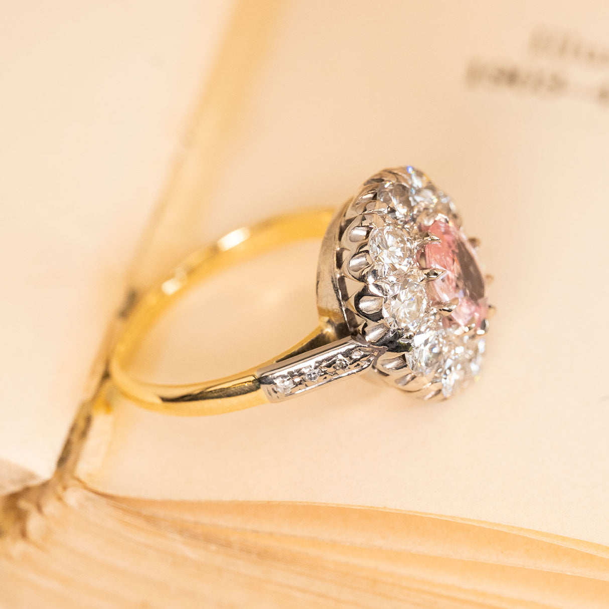 Orange-pink sapphire and diamond cluster ring showcasing a vibrant oval sapphire framed by sparkling diamonds in a classic white and yellow gold setting.