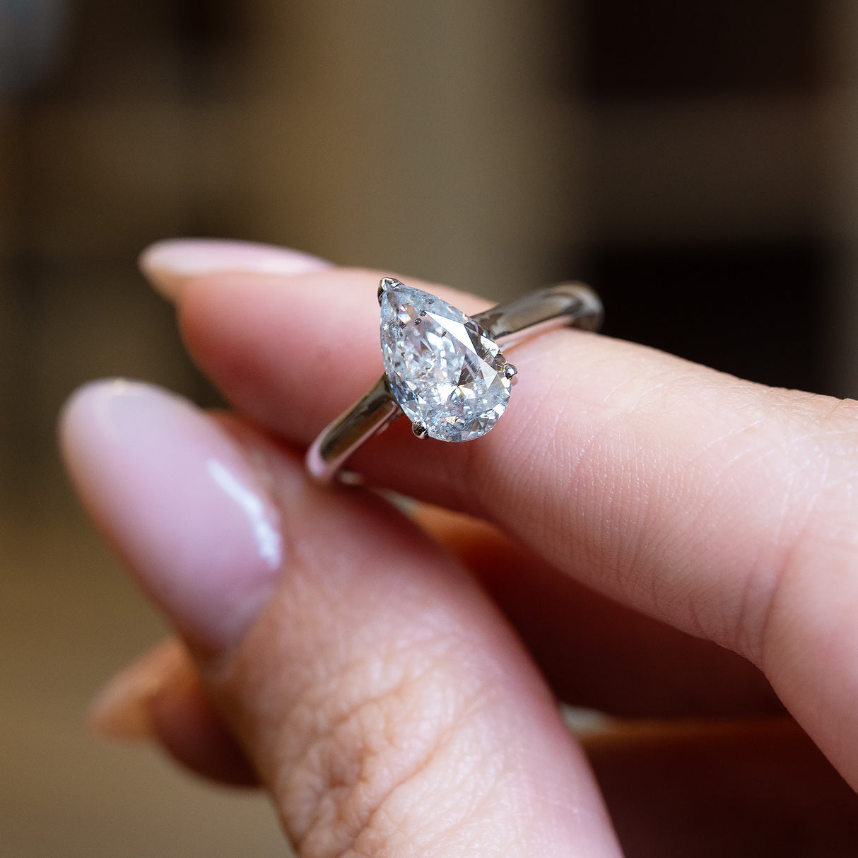 Vintage salt and pepper diamond solitaire ring held between fingers showing pear-shaped diamond detail.