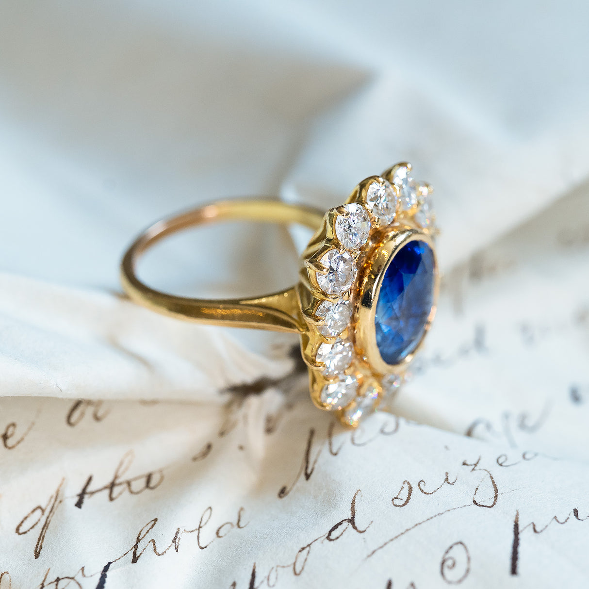 Vintage sapphire and diamond cluster ring with oval blue sapphire framed by bright round diamonds.