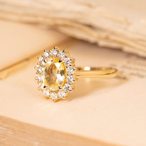 Vintage yellow sapphire and diamond halo ring showcasing a soft pastel yellow oval sapphire framed by a sparkling diamond cluster in yellow gold.