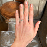 Yellow gold three-stone engagement ring featuring round green sapphire centre and diamond side stones, worn on hand.