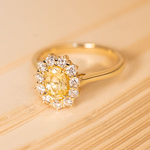 Oval-cut yellow sapphire engagement ring with a warm golden centre stone encircled by bright diamonds in an elegant antique-inspired setting.