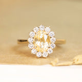 Yellow sapphire and diamond cluster engagement ring with oval-cut yellow sapphire in yellow gold.