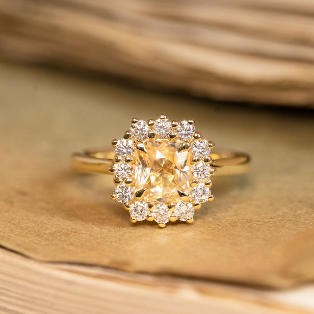 Yellow sapphire and diamond cluster engagement ring featuring a radiant yellow sapphire surrounded by brilliant-cut diamonds in yellow gold.