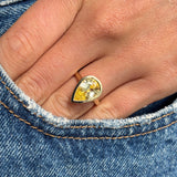 Antique-inspired yellow gold solitaire ring with a large pear-cut Sri Lankan yellow sapphire, styled on hand against blue denim to highlight the gemstone's vivid colour and elegant proportions.