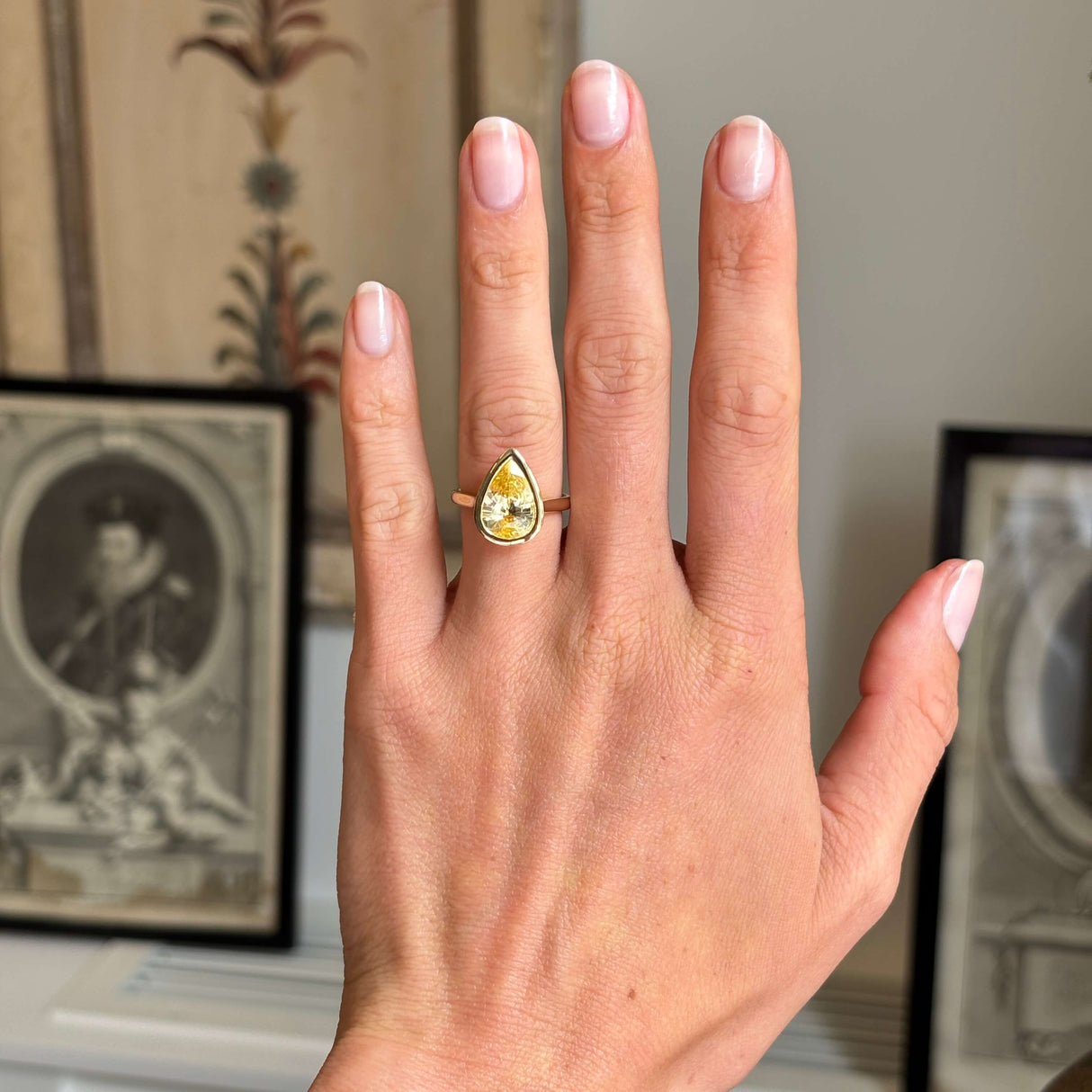 Antique-inspired yellow gold solitaire ring worn on hand, featuring a large pear-cut Sri Lankan sapphire in a sleek rub-over setting with vibrant golden-yellow colour.