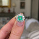 Edwardian emerald and diamond cluster ring, held in fingers and rotated to give perspective.