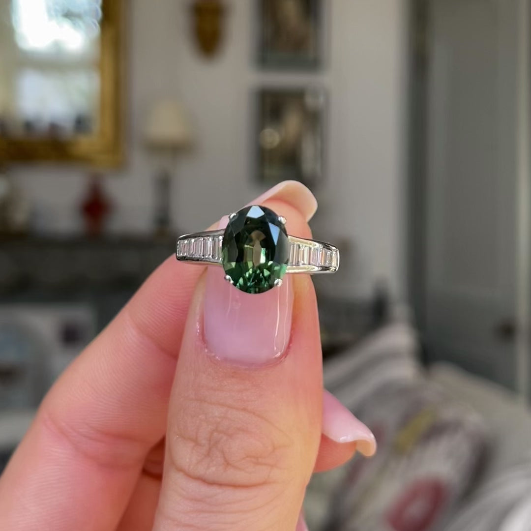 Green sapphire and diamond engagement ring held in fingers and moved around to give perspective.