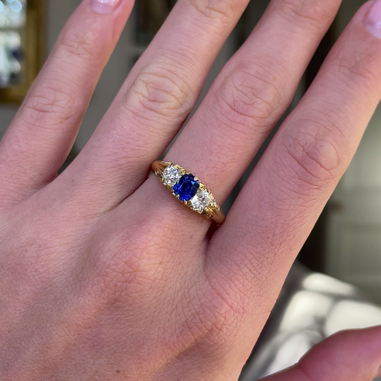 Sapphire and diamond three stone ring, worn on hand and rotated to give perspective.