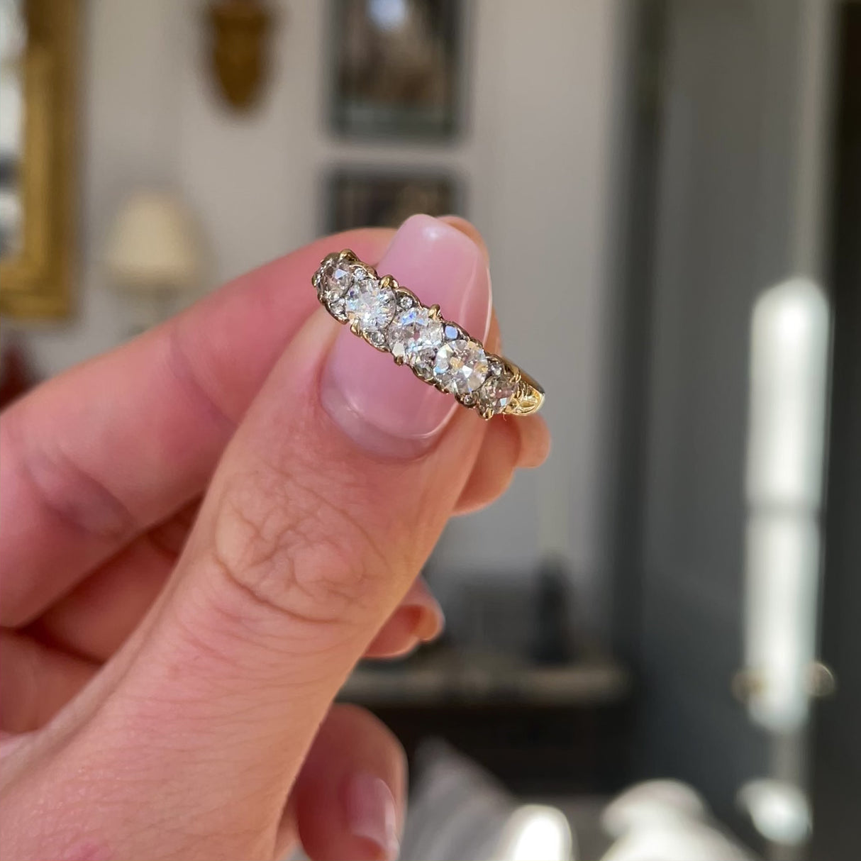 Antique five-stone diamond engagement ring, held in fingers and rotated to give perspective.