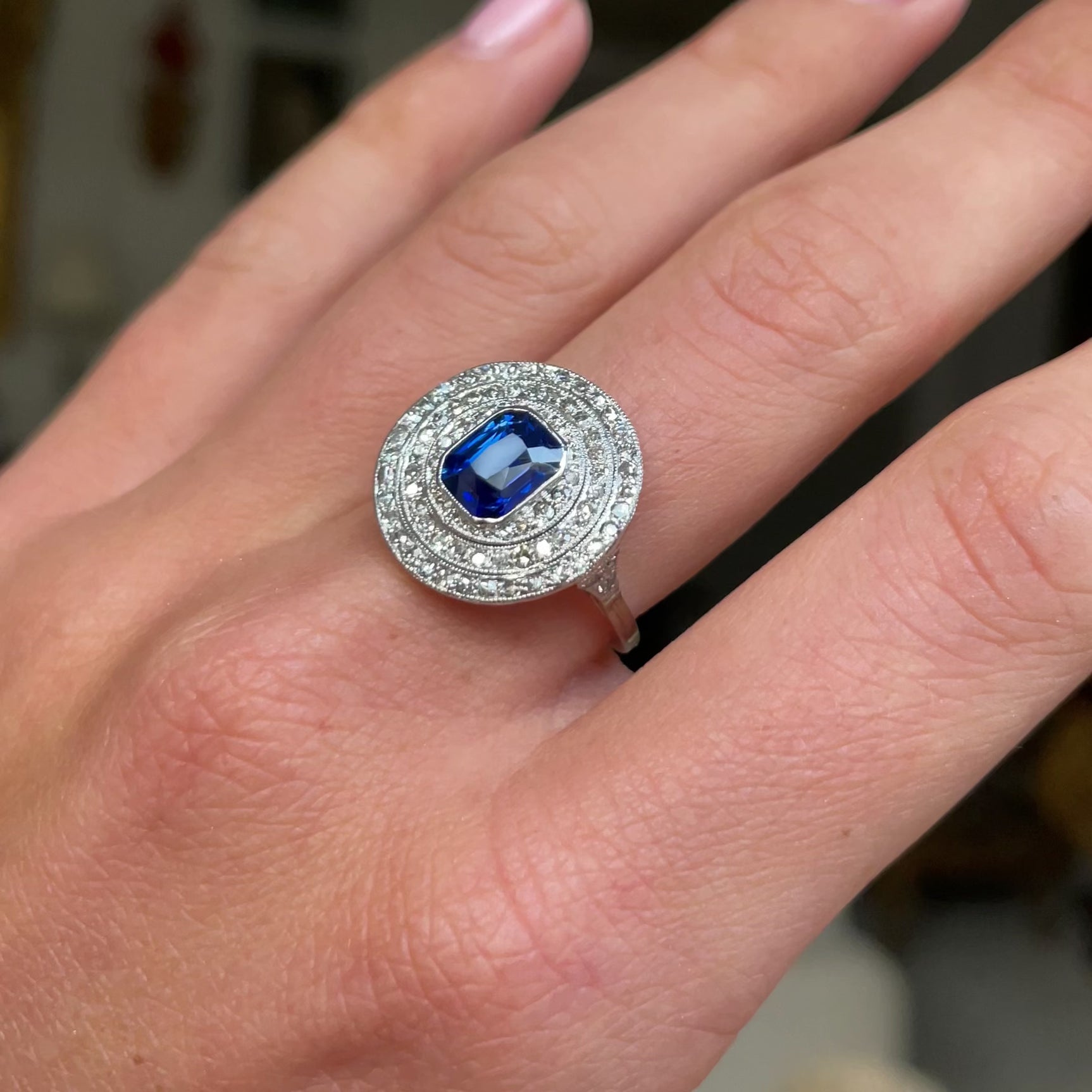 Sapphire and diamond target cluster ring, worn on hand and moved around to give perspective.