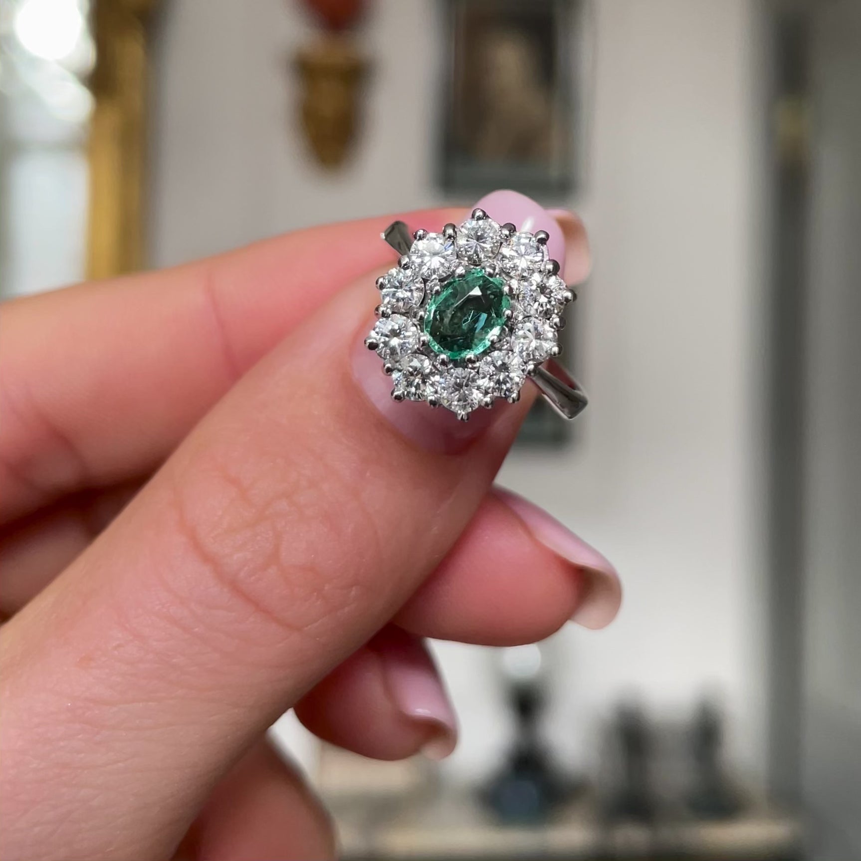 Austrian emerald and diamond cluster engagement ring, held in fingers and moved around to give perspective.
