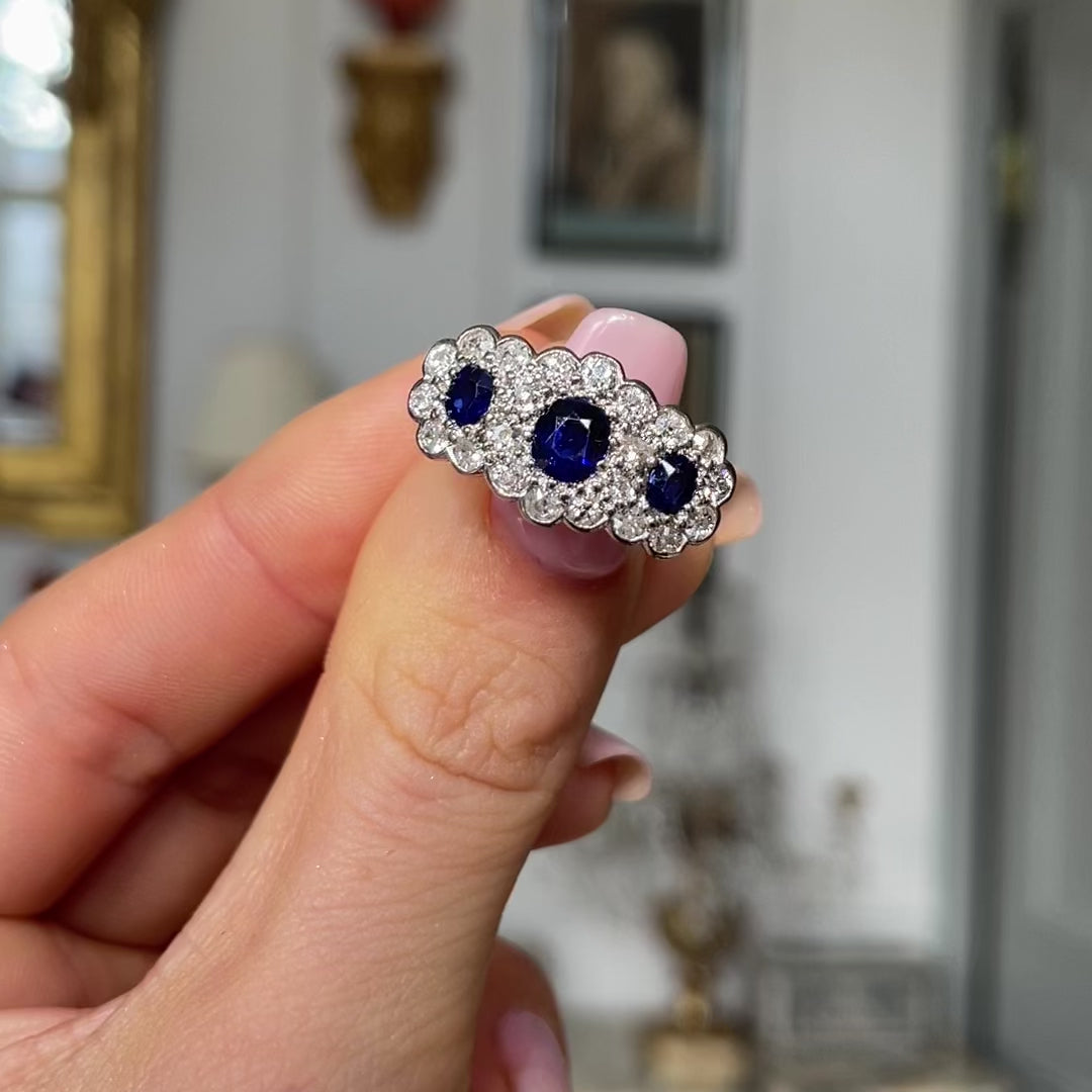 Antique sapphire and diamond triple cluster ring, held in fingers and moved around to give perspective.
