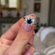 sapphire and diamond cluster engagement ring, held in fingers and rotated to give perspective.