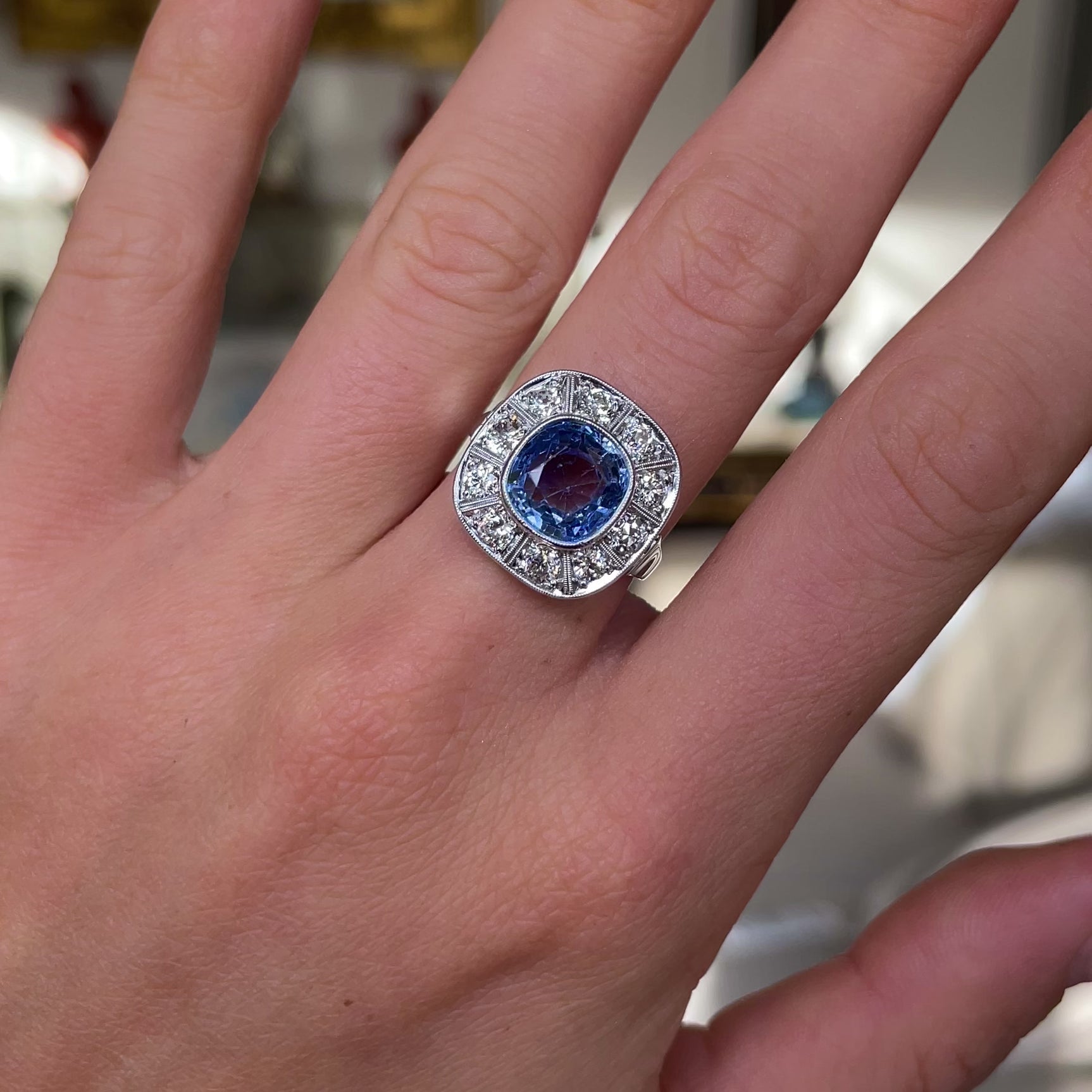 Art Deco, ceylon cushion-cut sapphire and diamond cluster ring, worn on hand and rotated to give perspective.