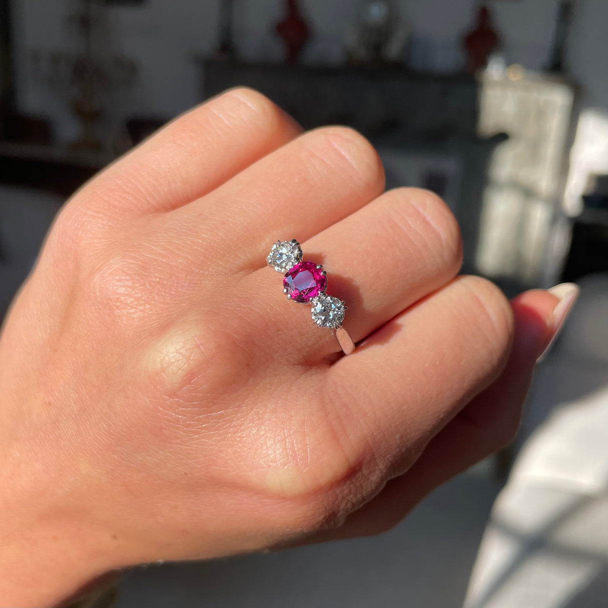 Ruby and diamond three-stone engagement ring, worn on hand.