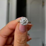 Vintage Art Deco white gold diamond cluster engagement ring, held in fingers.