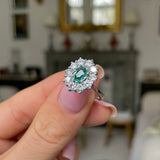 Austrian emerald and diamond cluster engagement ring, held in fingers.