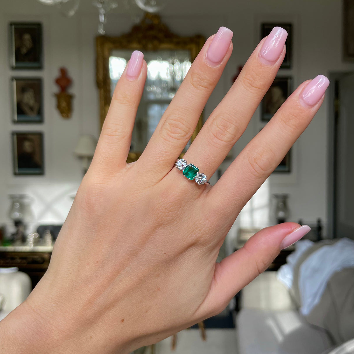 Vintage Art Deco three-stone emerald and diamond engagement ring, worn on hand.