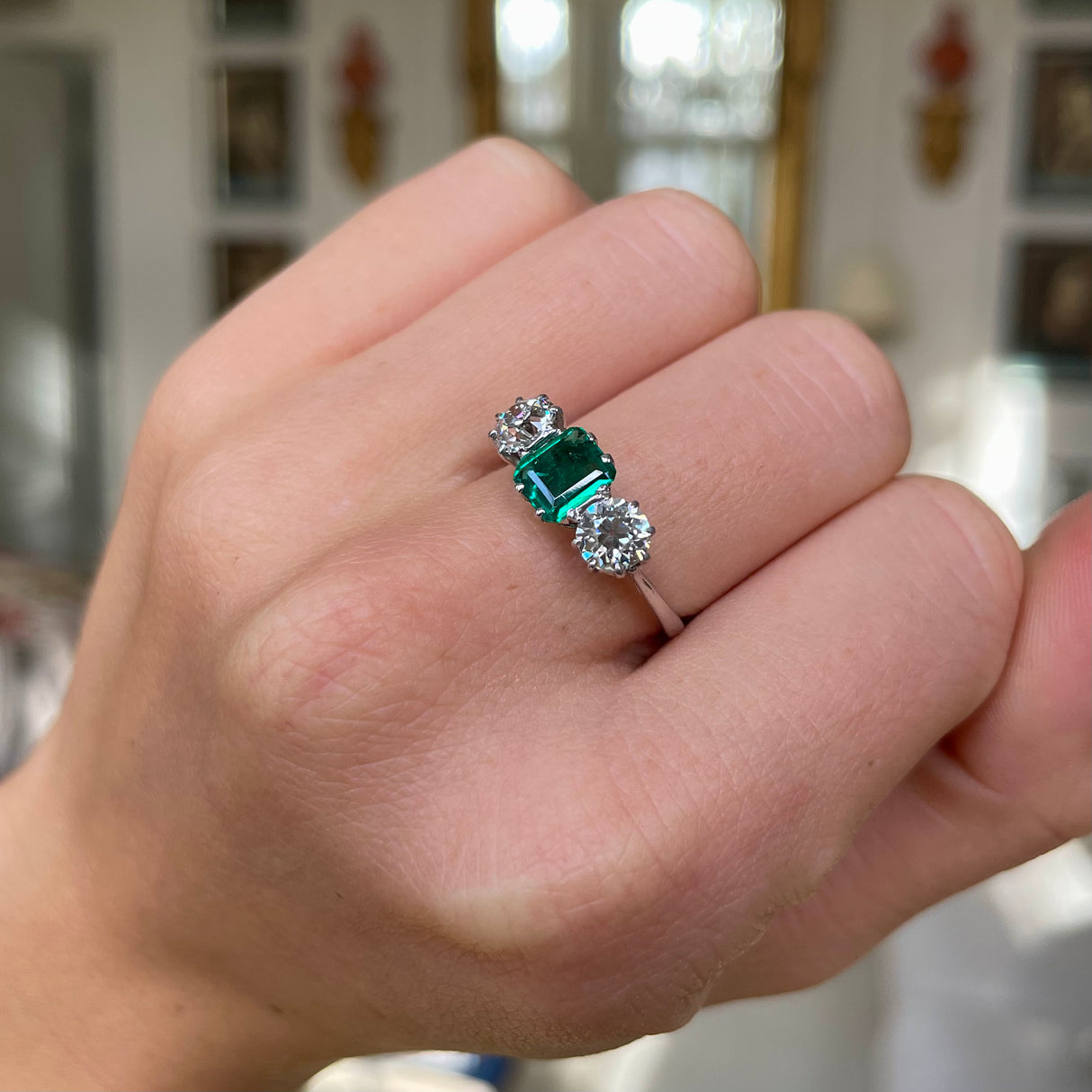 Vintage Art Deco three-stone emerald and diamond engagement ring, worn on hand.