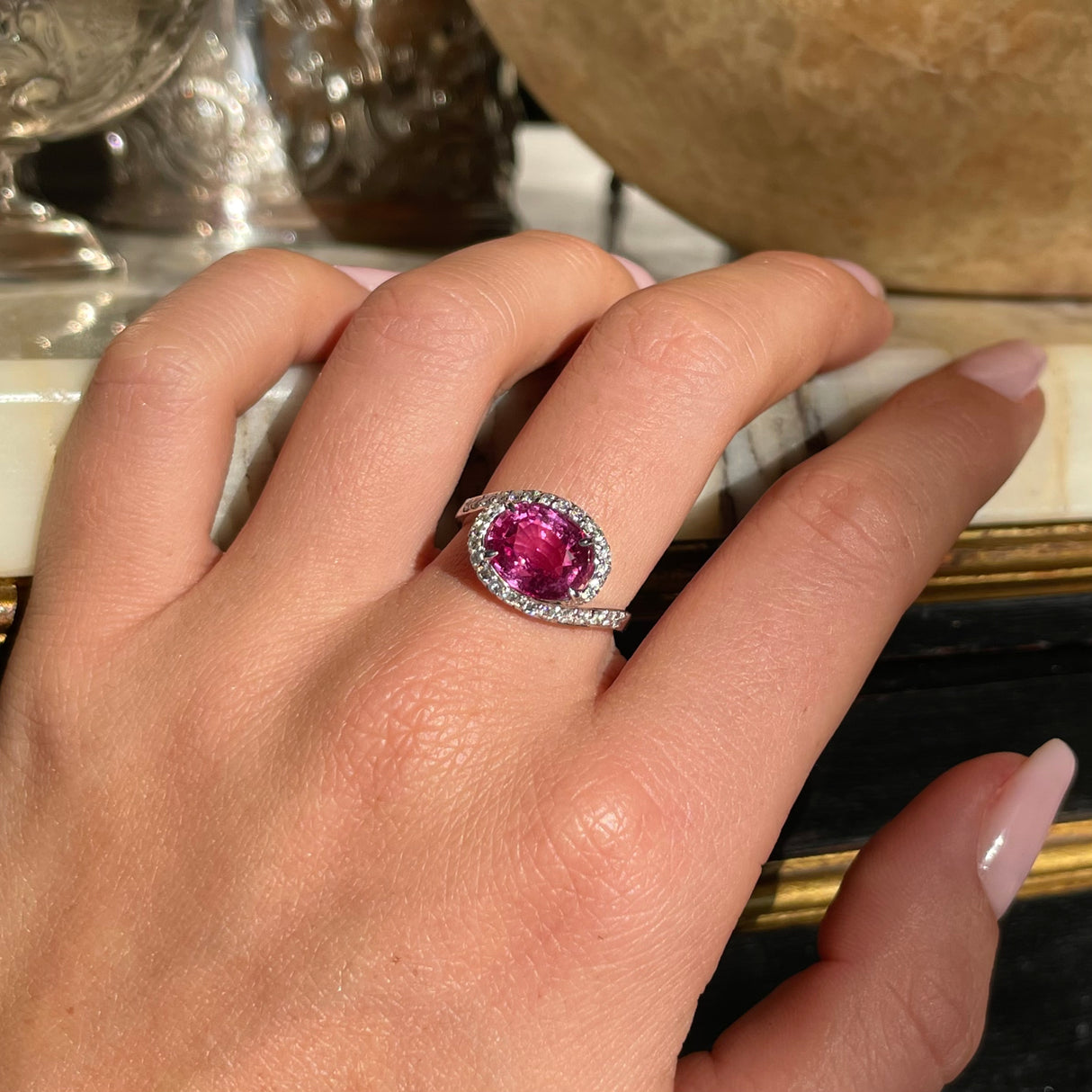 Pink sapphire and diamond engagement ring, worn on hand.