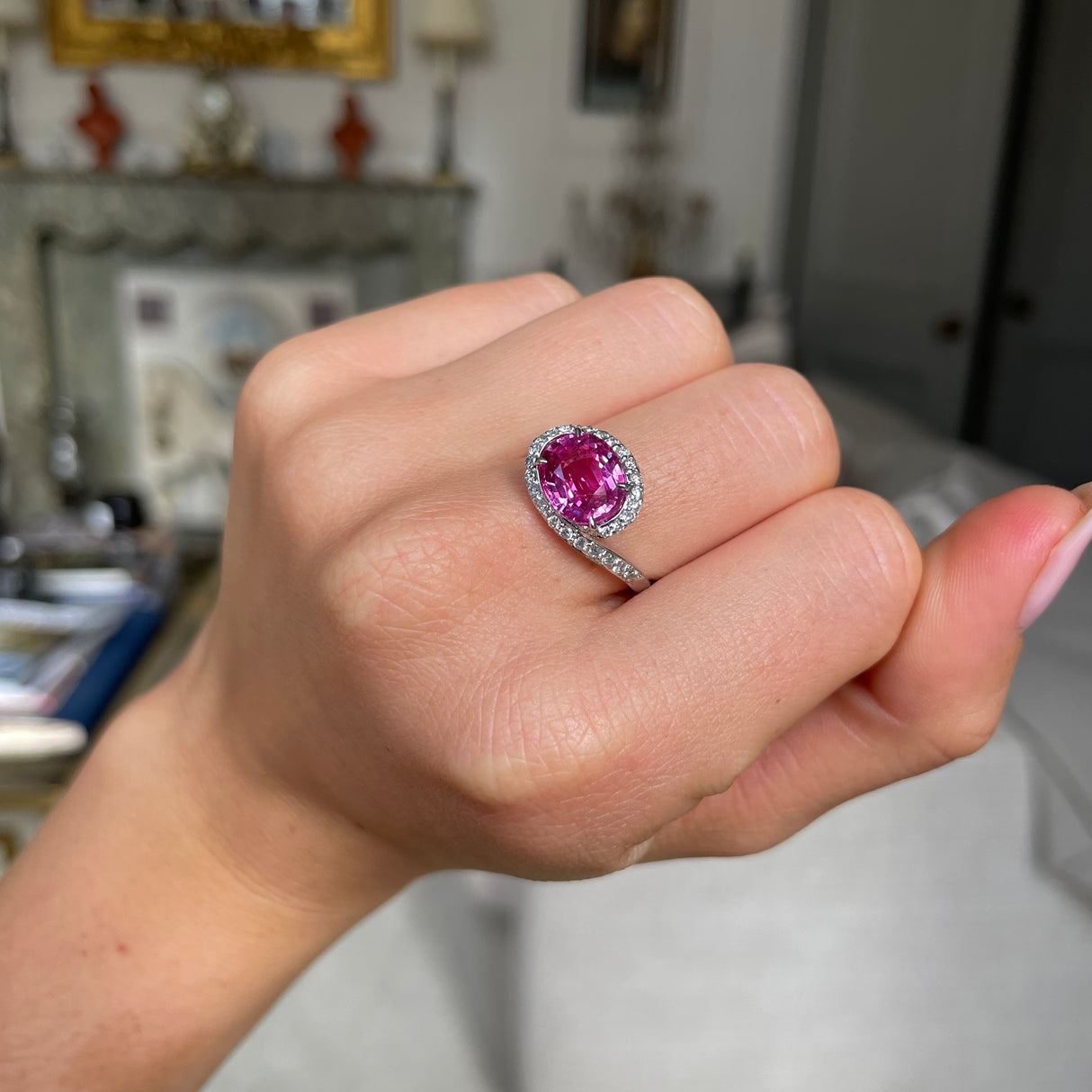 Pink sapphire and diamond engagement ring, worn on closed hand.