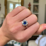 sapphire and diamond cluster engagement ring, worn on hand.