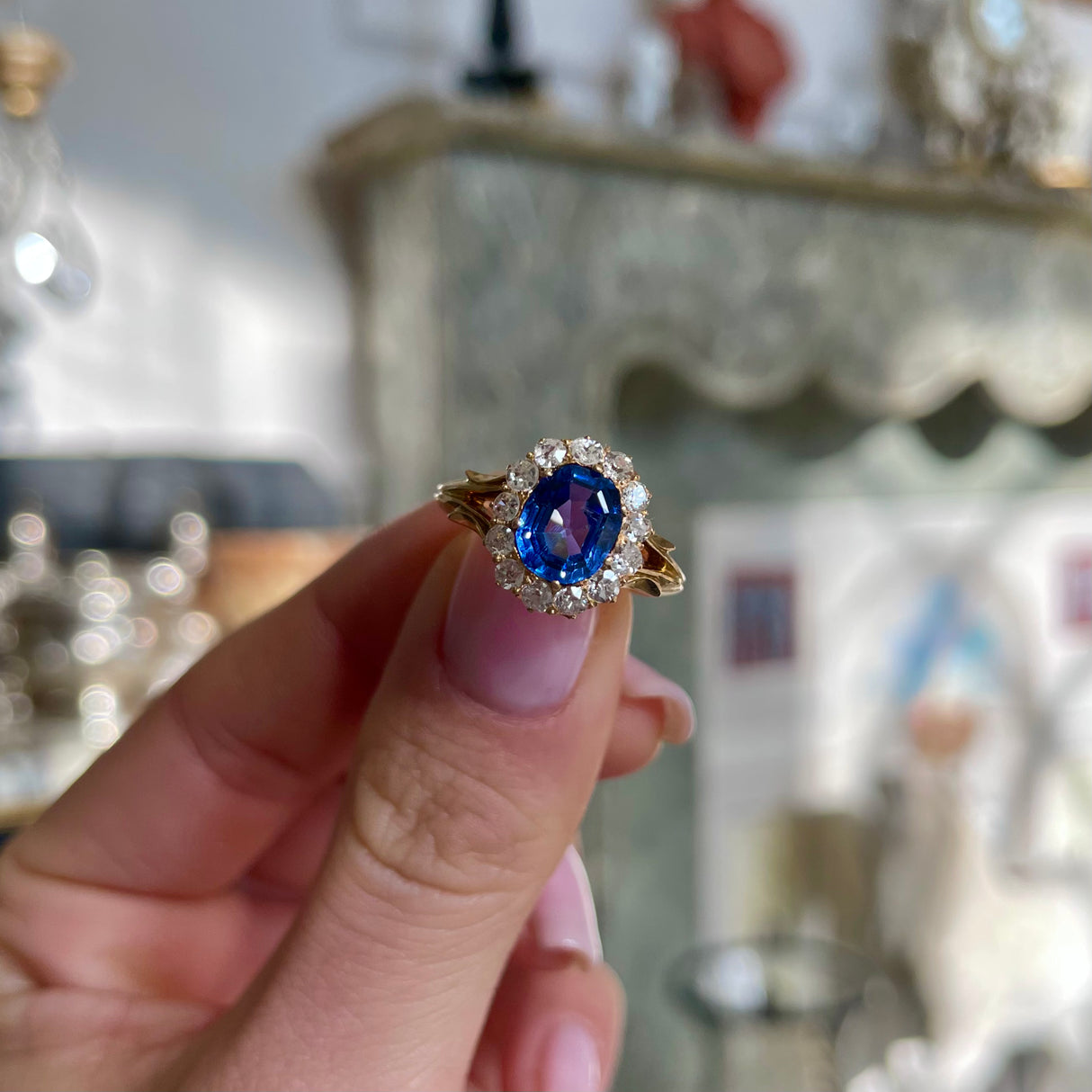 Victorian, sapphire and diamond cluster engagement ring, held in fingers.