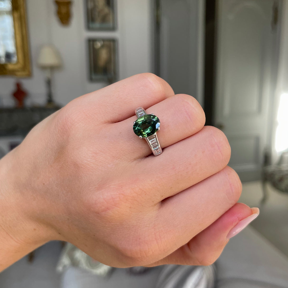 Green sapphire and diamond engagement ring worn on closed hand.