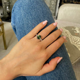 Green sapphire and diamond engagement ring worn on hand on jeans.