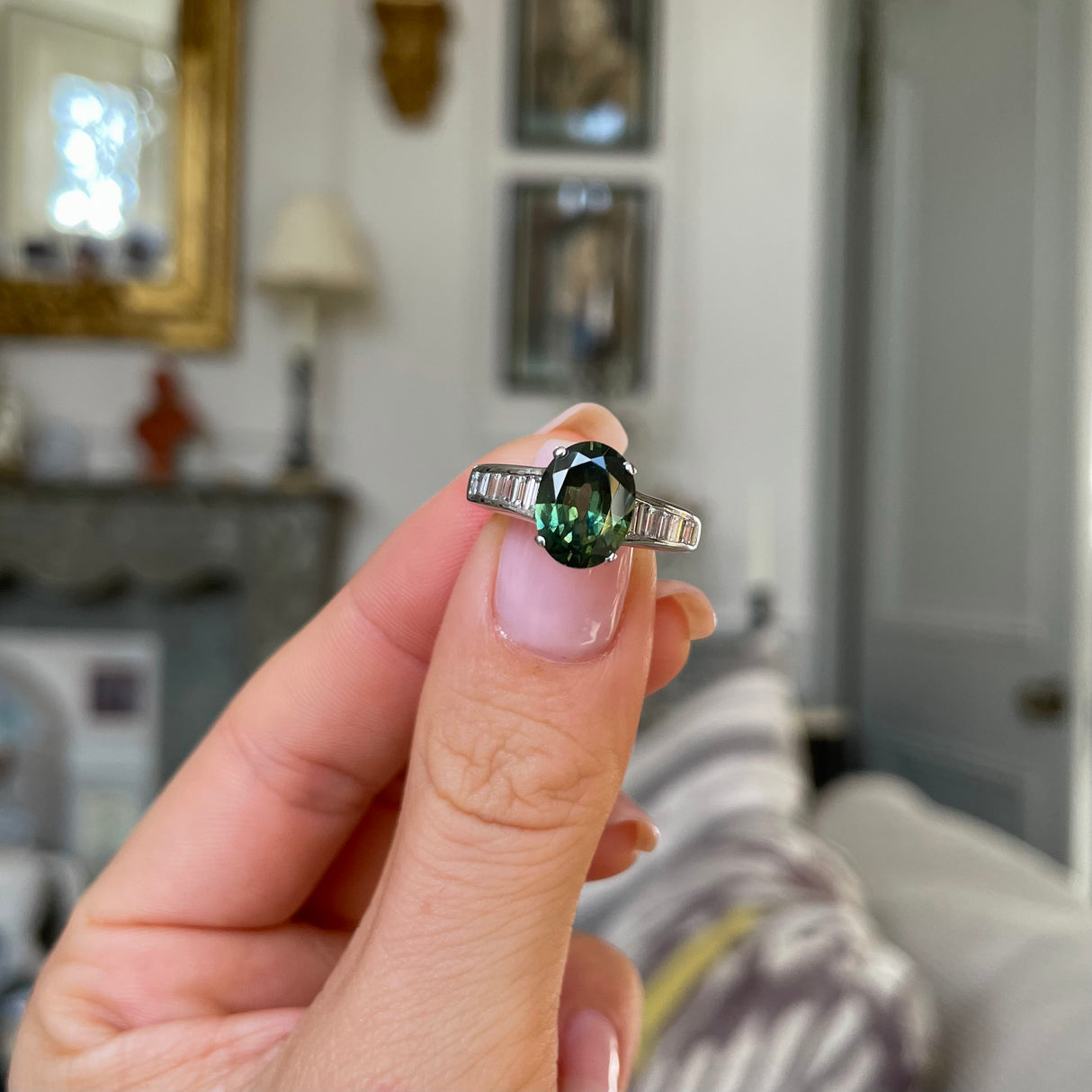 Green sapphire and diamond engagement ring held in fingers.