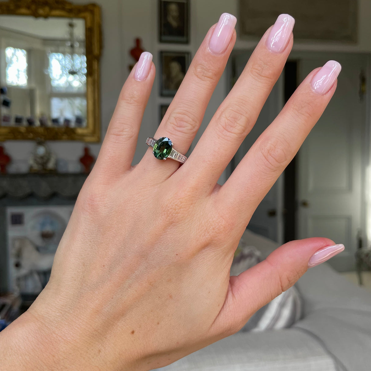 Green sapphire and diamond engagement ring worn on hand.