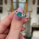 Vintage Art Deco three-stone emerald and diamond engagement ring, held in fingers and rotated to give perspective.