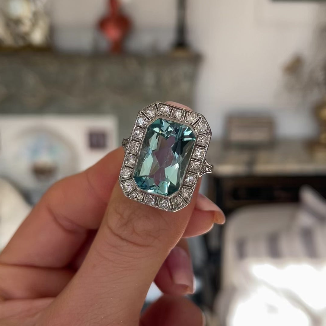 Art Deco aquamarine and diamond cluster ring, held in fingers and moved around to give perspective.